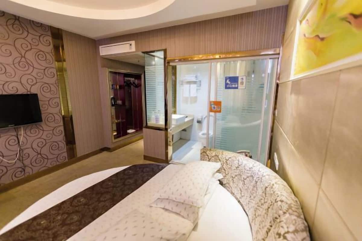 Een hotelkamer met een bed, een televisie, een badkamer met een glazen douche en een receptie.