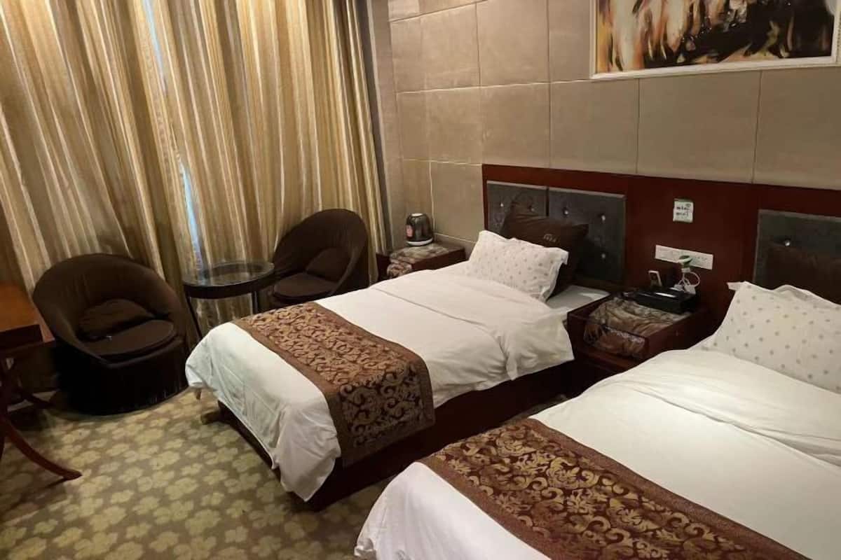 Een hotelkamer met twee bedden, een stoel, een kleintje tafeltje en een schilderij aan de muur.