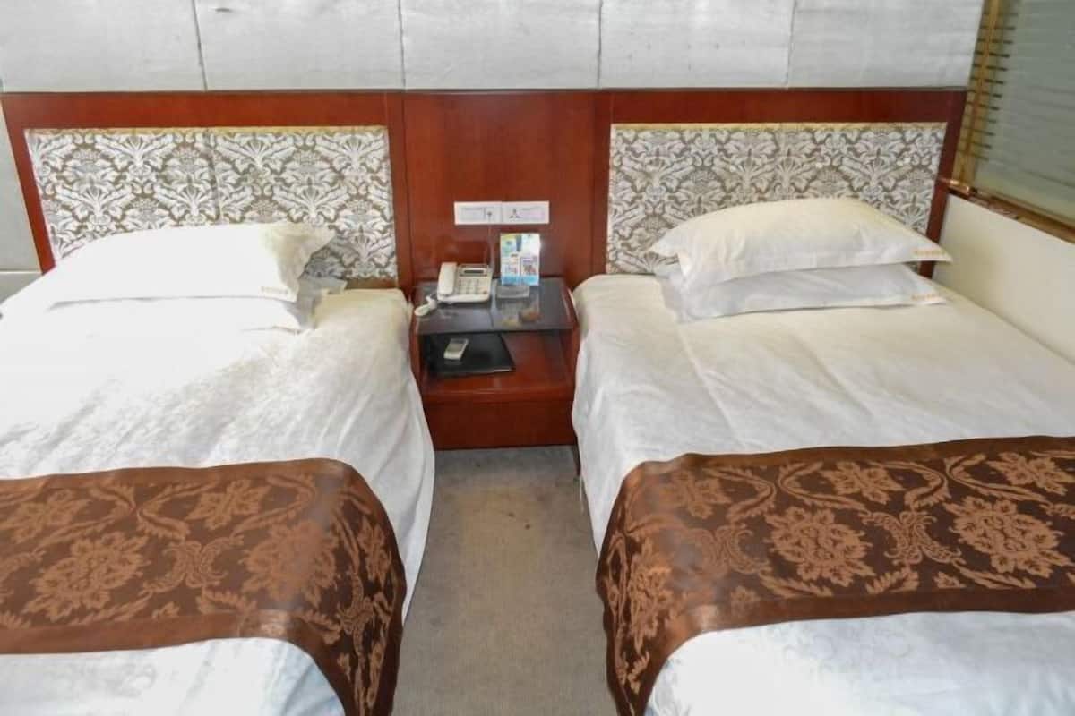 Een hotelkamer met twee bedden, een nachtkastje met een telefoon en een tijdschrift, en gestreept bedhoofd.