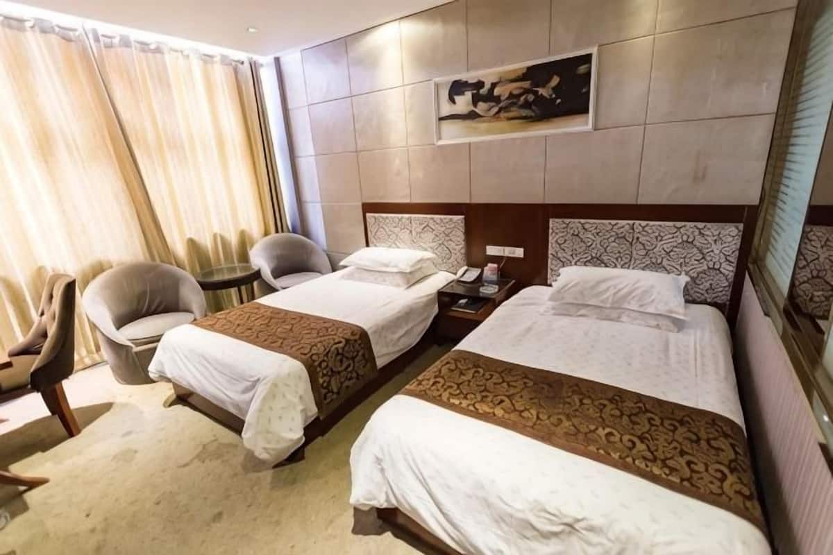 Een hotelkamer met twee bedden, een bureau, een stoel en een raam met gordijnen.