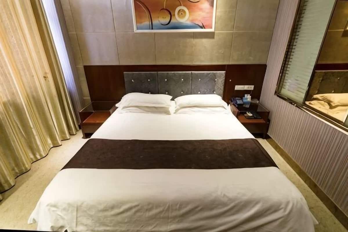 Een hotelkamer met een groot bed, een hoofdeinde, een nachtkastje, een raam en een schilderij aan de muur.