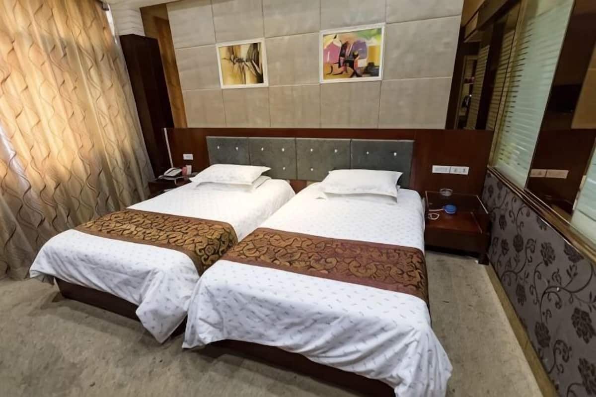Een tweepersoonsbed met een houten hoofdbord, twee nachtkastjes en een gordijn aan de linkerkant.