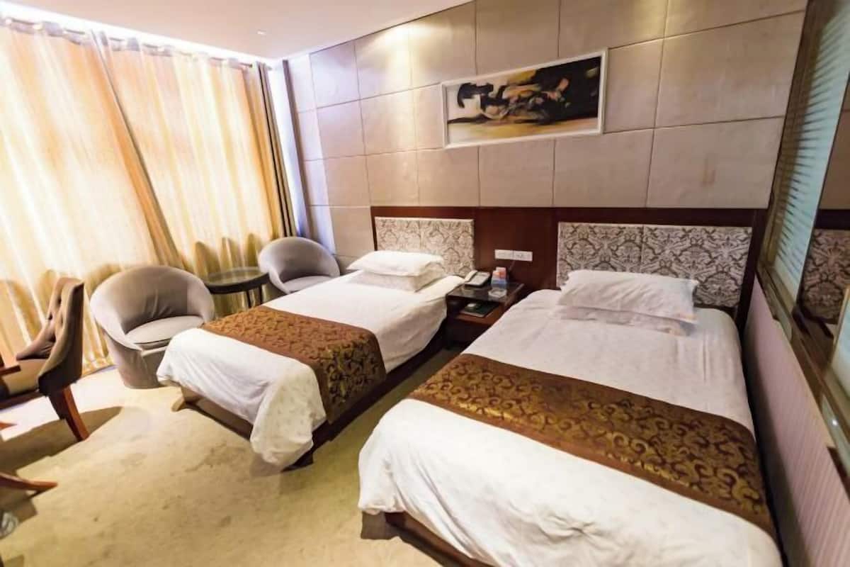 Een hotelkamer met twee bedden, een zithoek met stoelen, een nachtkastje met een lamp en een schilderij aan de muur.