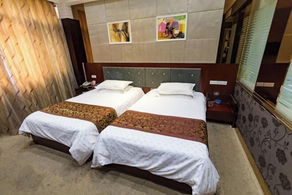 A hotel room with two beds, a headboard with artwork, a nightstand, and a window with blinds.