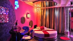 Un dormitorio moderno con una cama redonda, un espejo circular, una araña y una zona de bar.