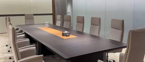 A conference room with a long table, six chairs, and a carpeted floor.