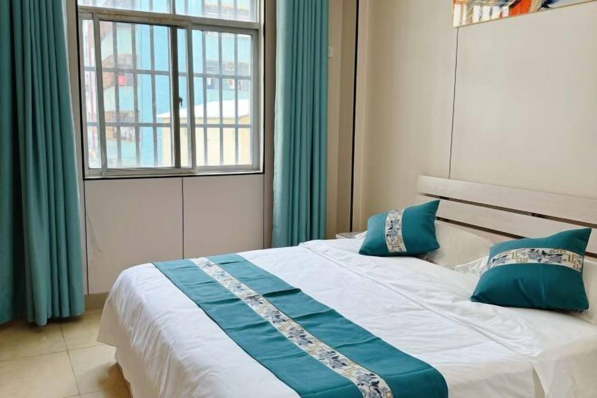 A hotel room with a bed, curtains, a window, and a wall unit.