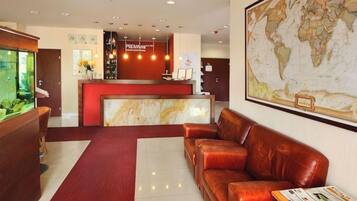 Un área de recepción con mostrador de mármol, alfombra roja, sofá de cuero y un mapa mundial en la pared.