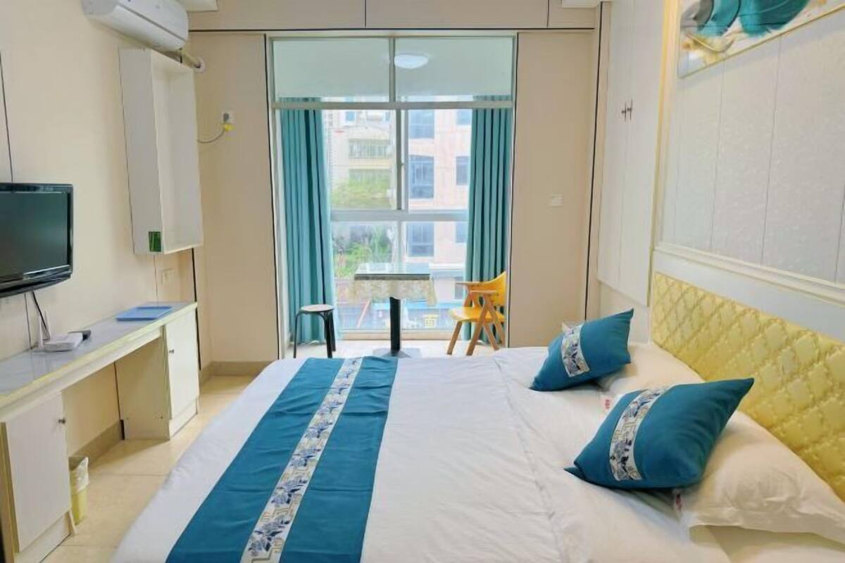 A hotel room with a bed, a desk, a television, a chair, and a view of buildings through the window.