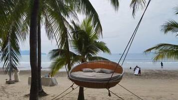 A beach setting with a hammock chair, palm trees, and a sandy beach.