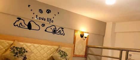 A hotel room with a bed, a headboard, a wall with a decorative phrase, and a light fixture.