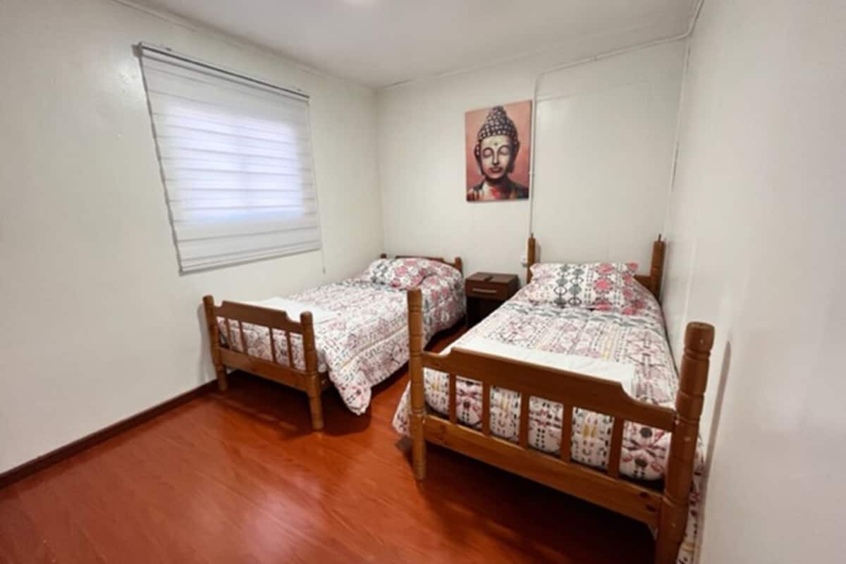 Un dormitorio con dos camas de madera, una ventana con persianas y una estatua de Buda en la pared.
