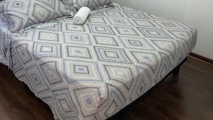 Un dormitorio con una colcha estampada, un cabecero, un cuadro en la pared y una ventana con persianas.