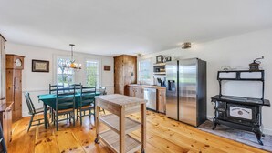 Una cocina con una mesa de madera, sillas, un refrigerador y una estufa antigua.