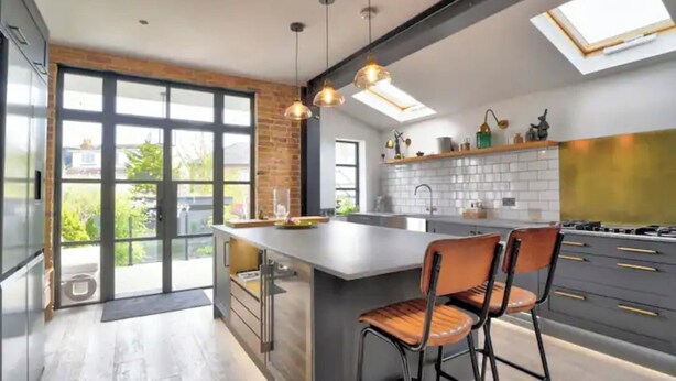 A modern kitchen with a large island, pendant lighting, and a view through the glass doors. - Stunning House in Leigh-on-sea (Leigh-on-Sea)