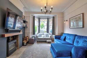 A living room with a fireplace, a blue sofa, a white sofa, and a TV mounted on the wall. - Stunning House in Leigh-on-sea (Leigh-on-Sea)