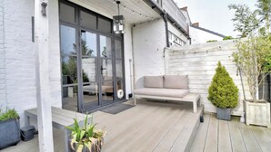 A modern patio with a cushioned seating area, a potted plant, and a sliding glass door leading to an interior space. - Stunning House in Leigh-on-sea (Leigh-on-Sea)