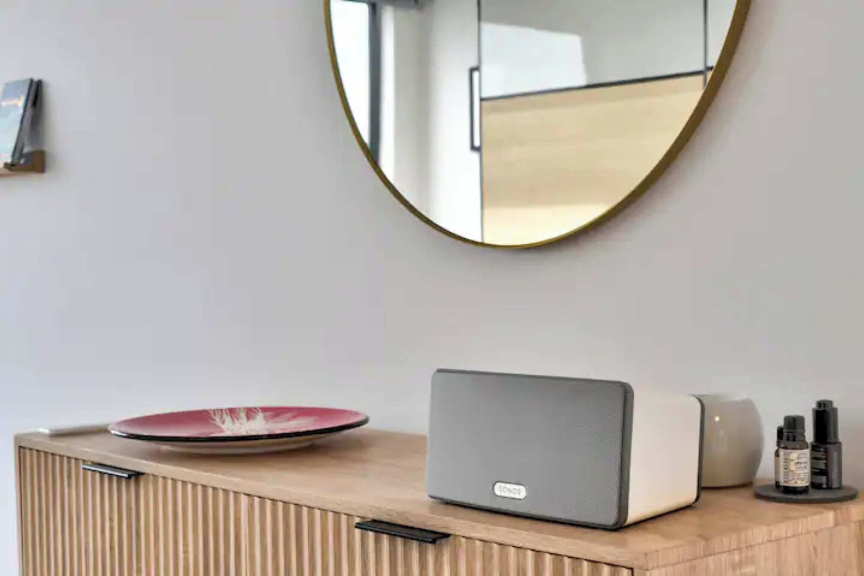 A modern room with a wooden cabinet, a laptop, a red plate, a speaker, and a round mirror on the wall.