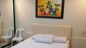 A hotel room with a bed, white pillows, a painting on the wall, and two white chairs. - Idmat Inn (Davao City)