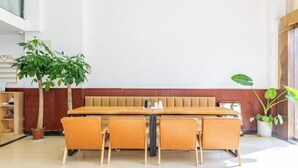 A dining area with a long wooden table and orange chairs, surrounded by potted plants. - Youth City Mini Hotel (Wuhan Institute of Engineering Science and Technology) (Wuhan)