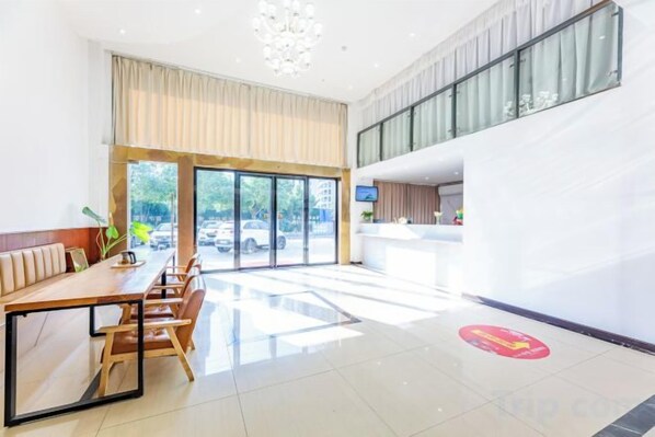 A hotel lobby with a reception desk, a seating area with a long table, and large windows offering a view of the outside. - Youth City Mini Hotel (Wuhan Institute of Engineering Science and Technology) (Wuhan)