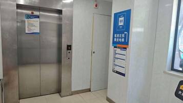 Um elevador com painel de controle e porta, uma placa na parede com texto e uma janela com vista.