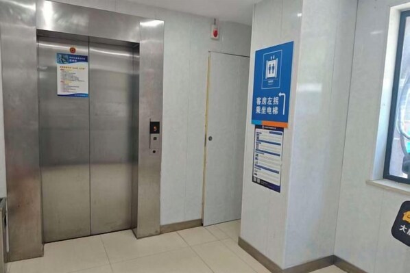 An elevator with a control panel and a door, a wall-mounted sign with text, and a window with a view.