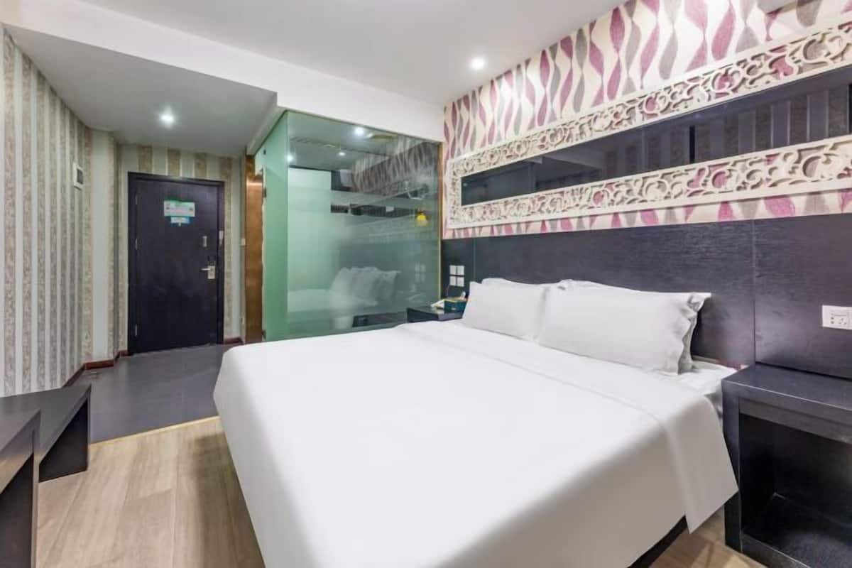 Une chambre d’hôtel avec un lit, un bureau, un miroir et un mur décoré de motifs.