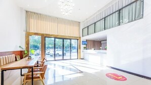 A modern hotel lobby with a reception desk, a seating area with a long table and chairs, and large windows offering a view of the outside. - Youth City Mini Hotel (Wuhan Institute of Engineering Science and Technology) (Wuhan)