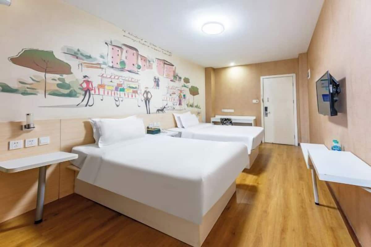 Une chambre d’hôtel avec deux lits, une petite table, un téléviseur fixé au mur et une fresque murale.