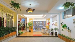 Un amplio vestíbulo de hotel con una zona de estar central, varias plantas en macetas y un moderno candelabro.