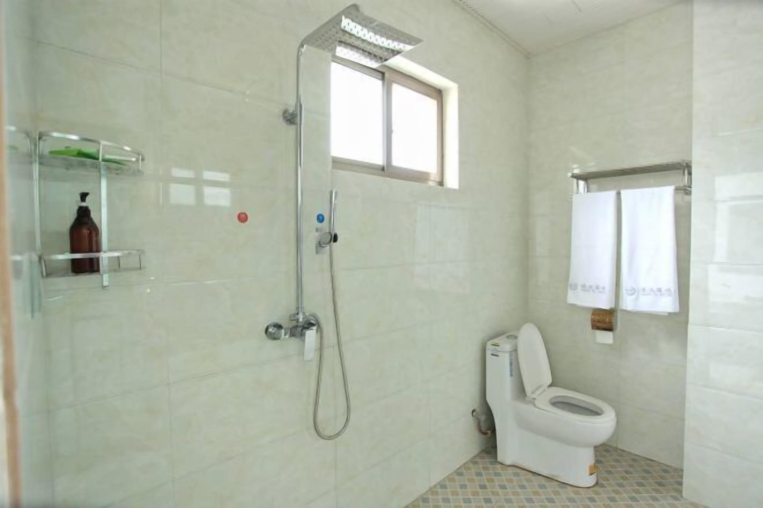 A bathroom with a shower, toilet, and a window.