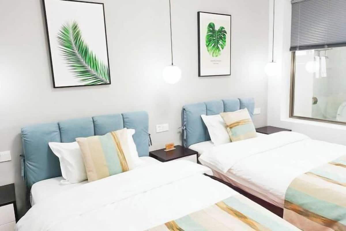 Une chambre d’hôtel avec deux lits, chacun doté d’une tête de lit bleue et de draps blancs. Des reproductions encadrées de motifs botaniques ornent le mur au-dessus des lits.