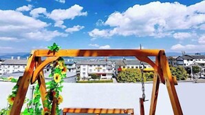 Un columpio de madera con un banco, con vista a un pueblo con edificios y un cielo despejado.