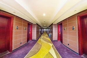 A hotel corridor with doors on both sides, a patterned carpet, and a ceiling with recessed lighting. - TianchengBusinessHotel (Luxi)