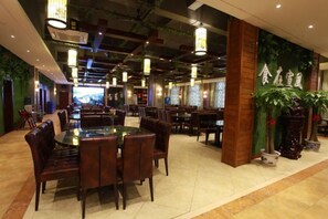 A restaurant with multiple dining tables and chairs, a green wall with plants, and hanging lights. - TianchengBusinessHotel (Luxi)
