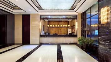 A hotel lobby with a reception desk, a chandelier, and a large window.