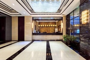 Un vestíbulo de hotel con mostrador de recepción, una araña y un ventanal grande.