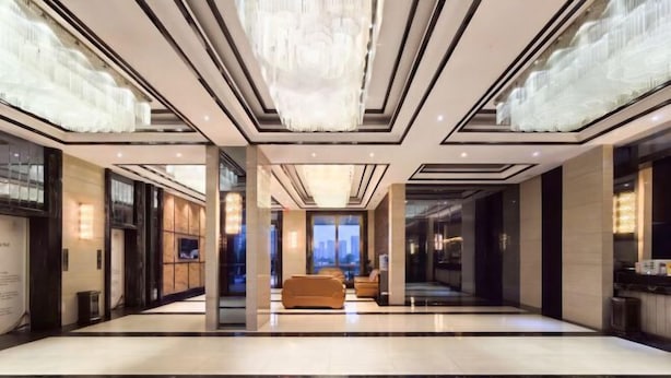 A spacious lobby with a modern chandelier, seating area, and large windows offering a city view. - TianchengBusinessHotel (Luxi)