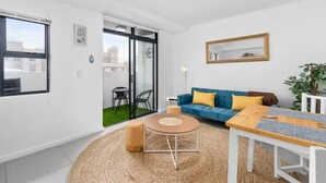 A modern living room with a blue sofa, a wooden coffee table, and a large window. - Beach Break Two - One Bedroom Apartment, Sleeps 2 (Cape Town)