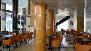A modern restaurant with high ceilings, wooden pillars, and orange chairs. - Hôtel La Luna (Beni Mellal)