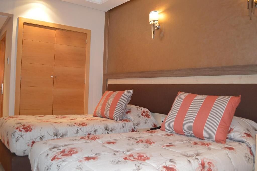 A bedroom with two beds, a wooden wardrobe, and a wall-mounted light fixture.