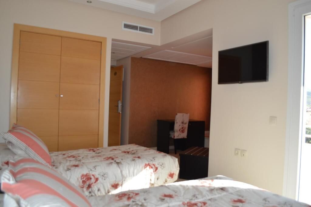 A bedroom with two beds, a TV mounted on the wall, and a wooden wardrobe.