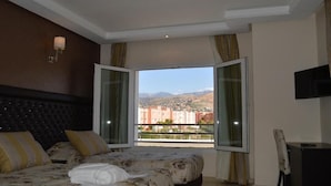A bedroom with a large bed, a TV, and a window with a view of buildings and mountains. - Hôtel La Luna (Beni Mellal)