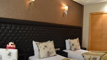 A hotel room with a tufted headboard, two beds with floral bedding, a nightstand, and a wooden wardrobe.