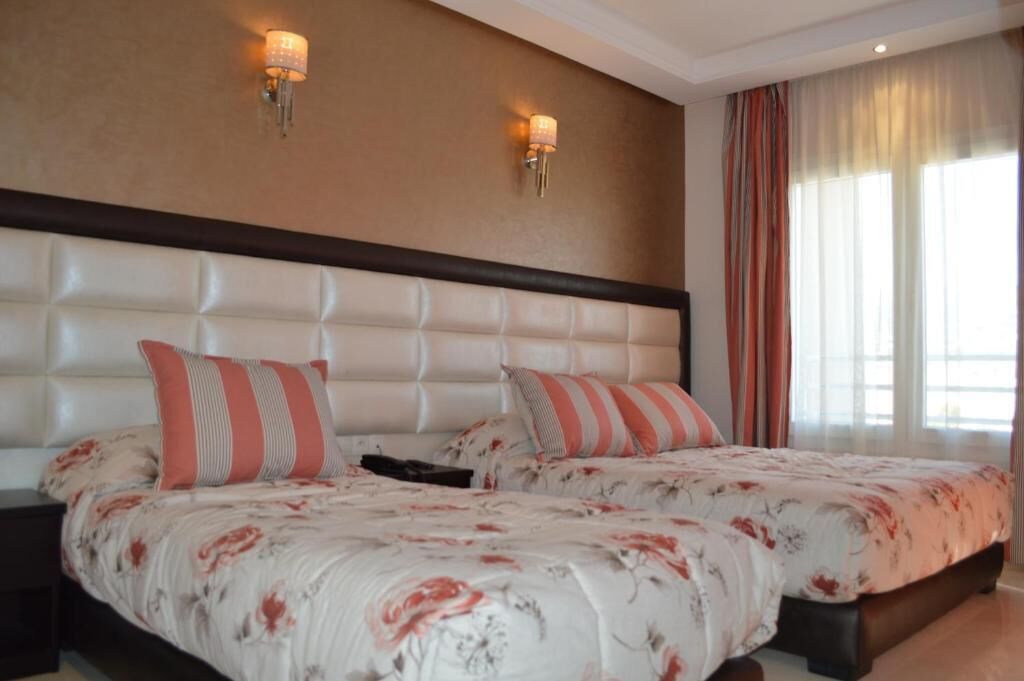 Una cama doble con ropa de cama floral, un cabecero capitonado y dos apliques de pared.