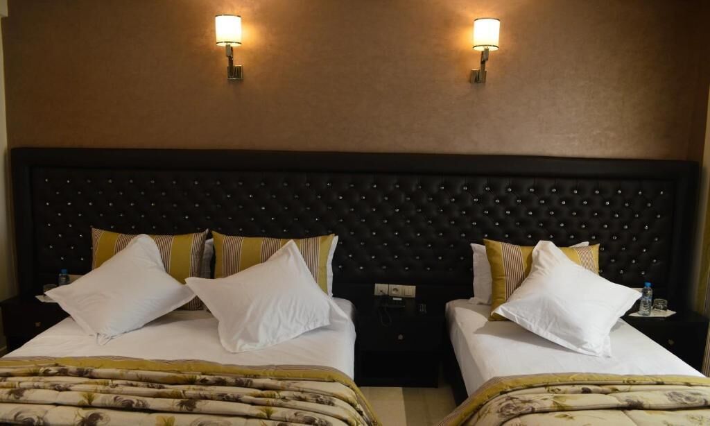 Une chambre d’hôtel avec deux lits, chacun agrémenté de draps blancs et d’oreillers à rayures. Des lampes murales sont fixées de chaque côté de la tête de lit.