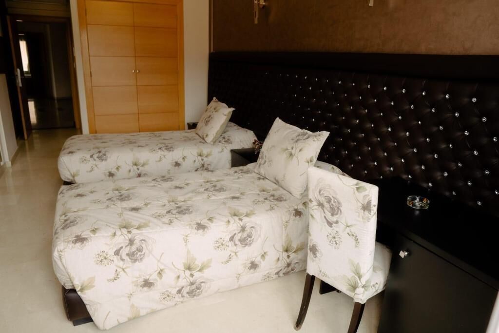 Una habitación de hotel con dos camas, cabecera oscura y un armario de madera.