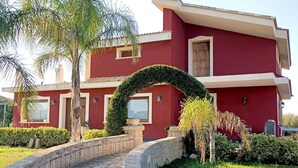 Una casa moderna de dos pisos amb façana vermella, un camí de pedra que porta a l'entrada i vegetació ben cuidada.