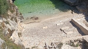 Una platja rocosa amb aigua cristal·lina i un pas estret entre penya-segats.